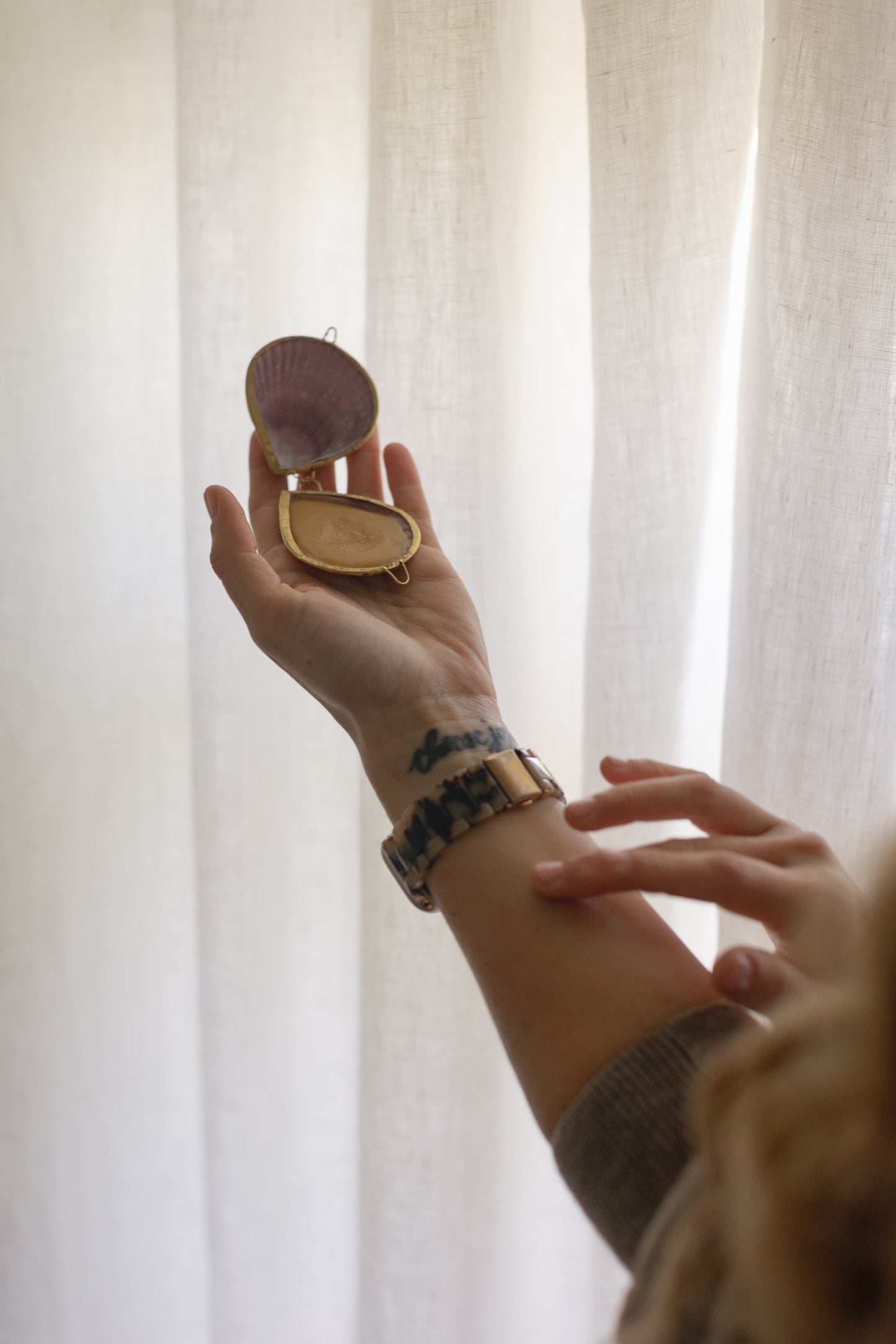 Picture of a hand touching the All Natural Jasmine Perfume inside a small container in form of a sea shell