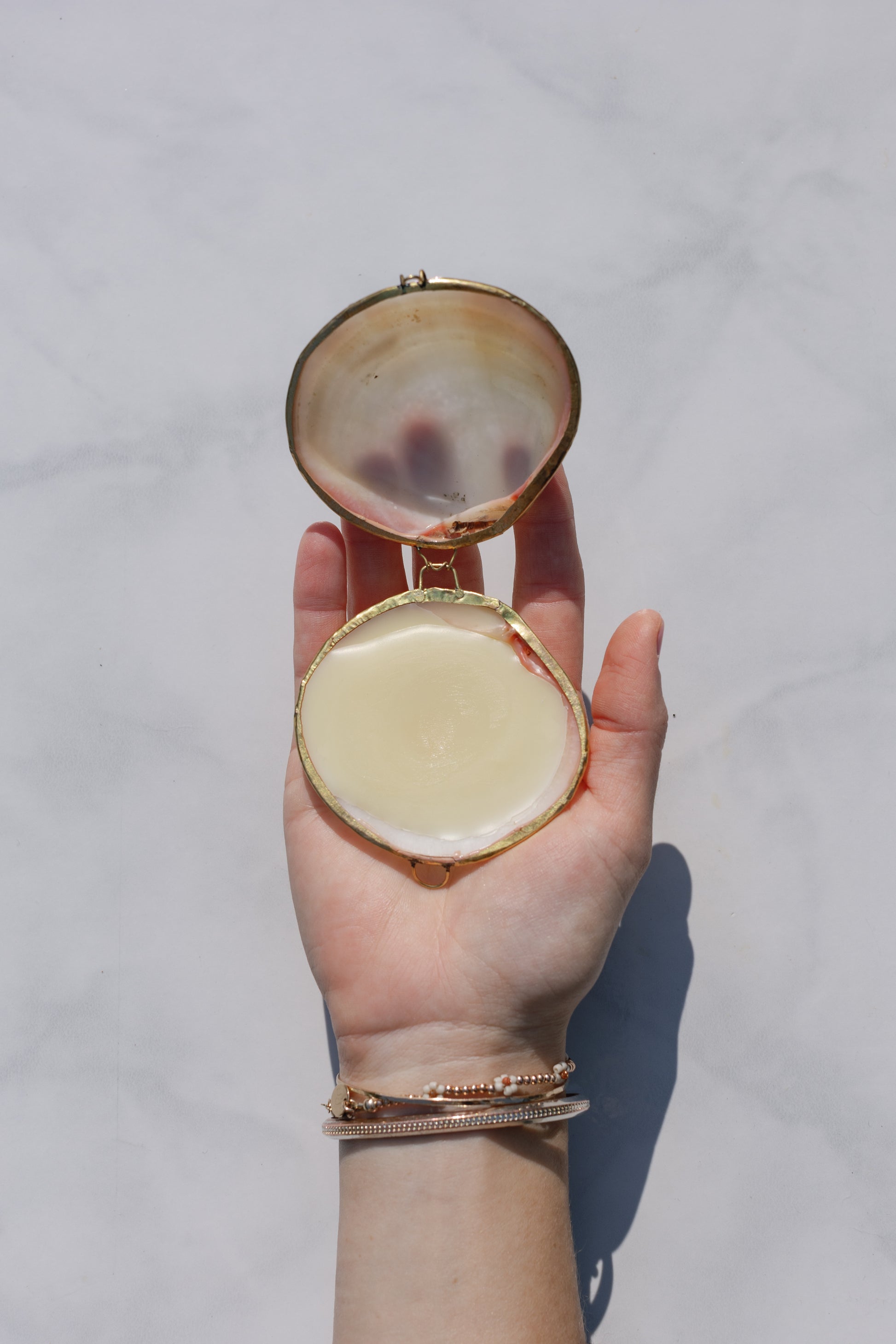 A hand holding the hydrating botanical balm packed in a small container in form of a sea shell