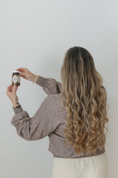 Picture of a blonde woman facing away while showing the Mane & Nails little container