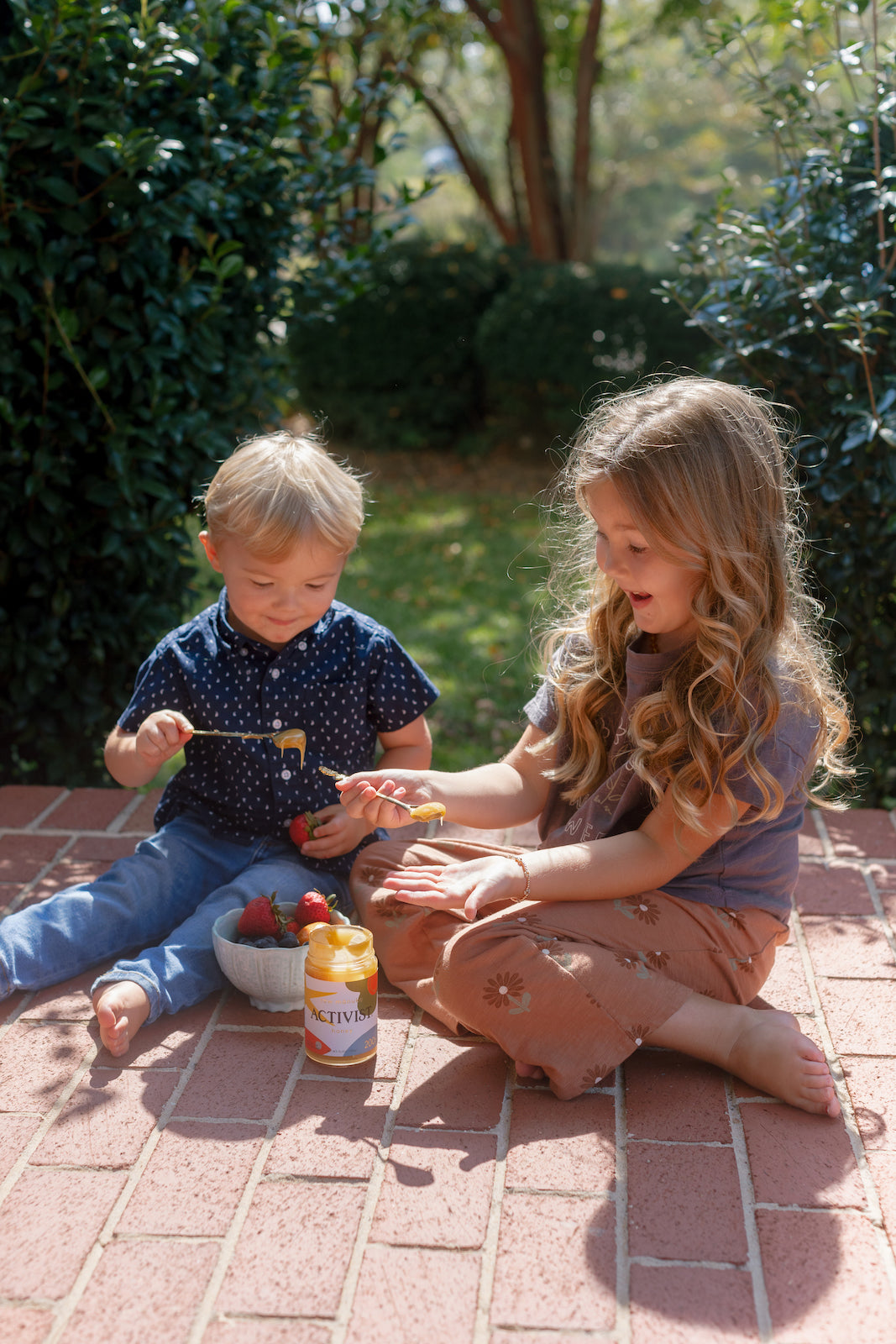 Picture of two small childs using spoons to put some Manuka Honey on some strawberries