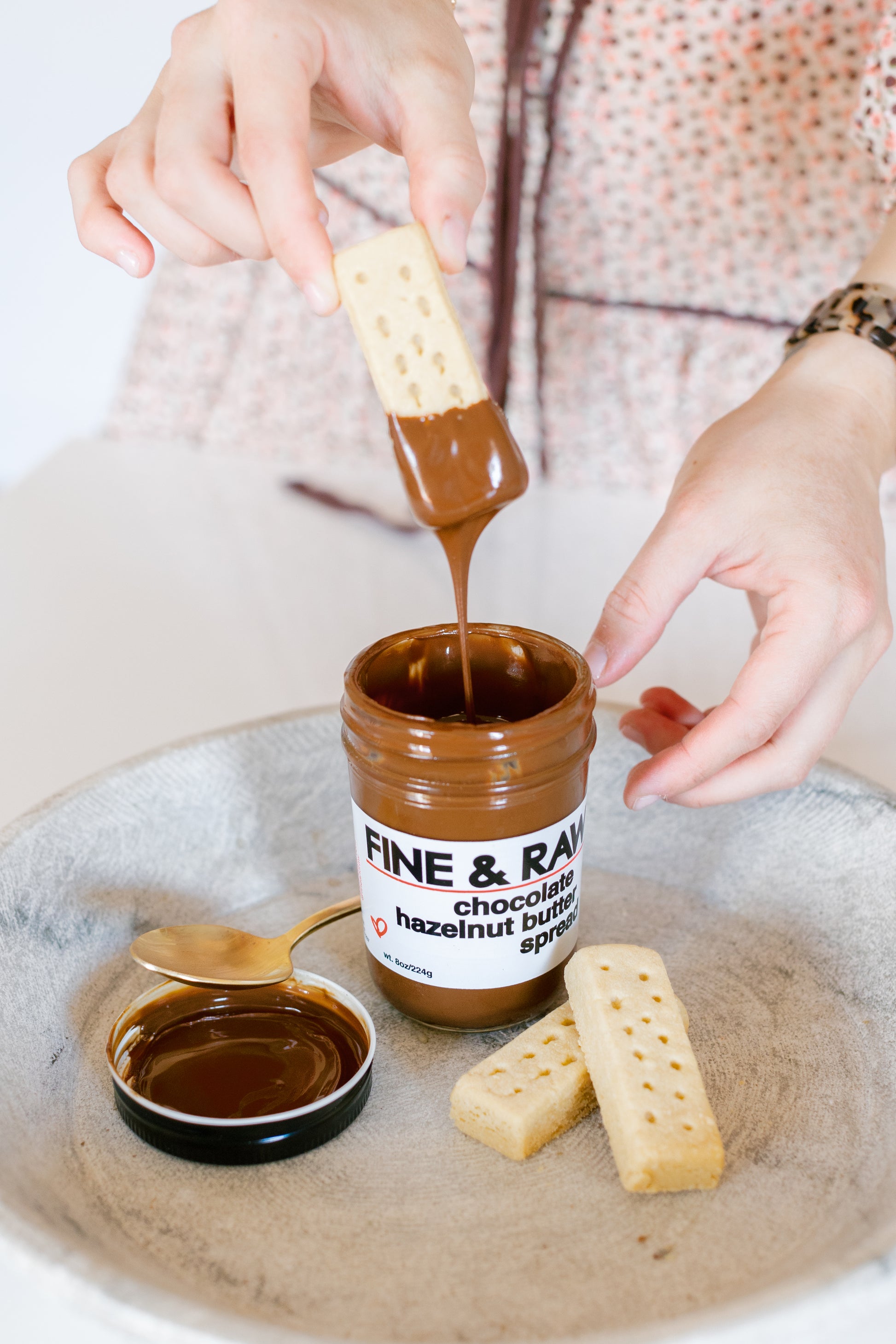 picture of a hand putting a biscuit inside the chocolate hazenlnut butter spread package