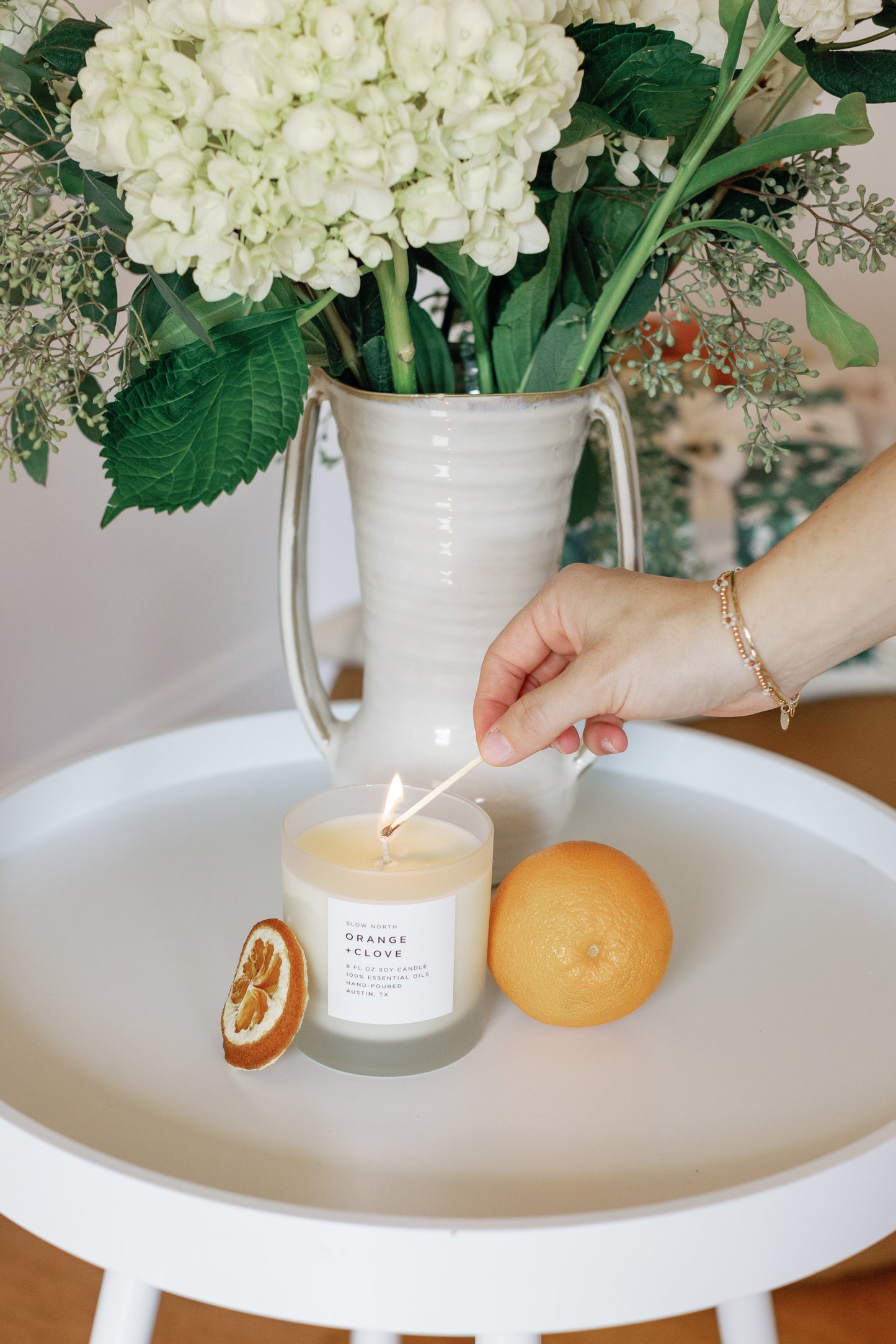 Image of a hand liting the Orange Clove Candle with a match