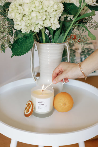 Image of a hand liting the Orange Clove Candle with a match