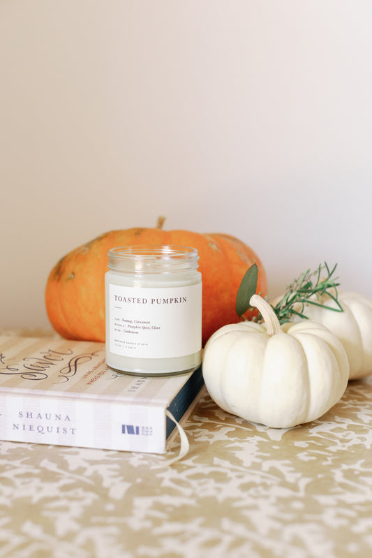 Image of a open Toasted Pumpkin Candle with some pumpkins behind it