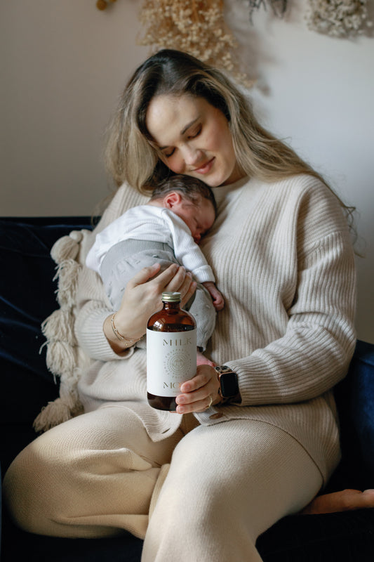 Image of Caroline holding her baby while holding the Postpartum Restorative Tonic with the other hand